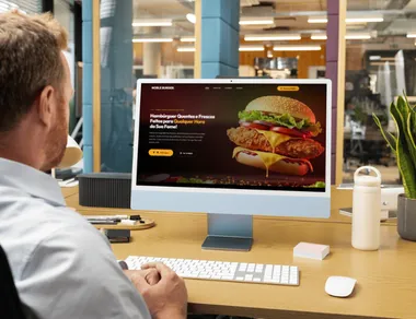 Profissional em mesa de trabalho olhando a home de um restaurante num iMac