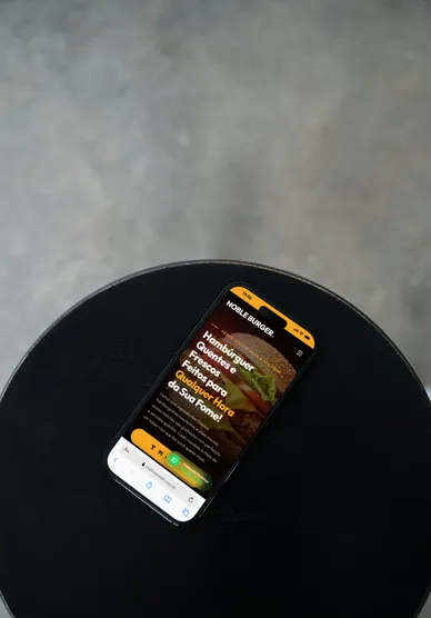 Smartphone sobre mesa escura mostrando o cardápio digital de uma hamburgueria, com o pedido em evidência